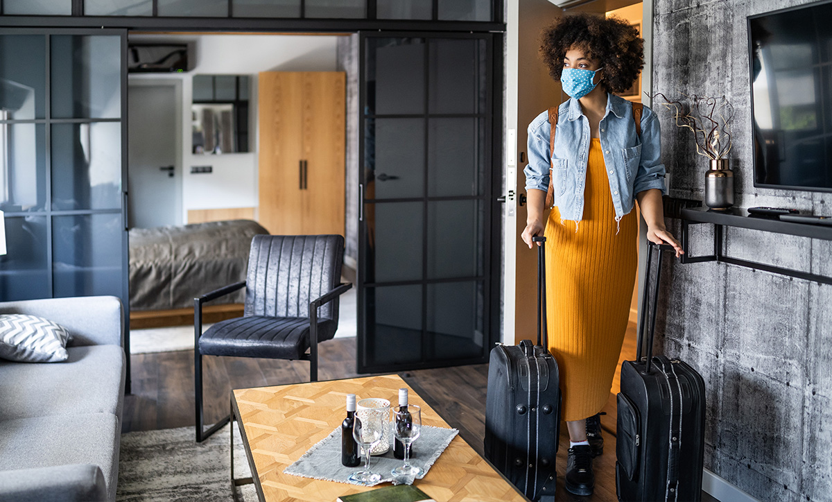 Covid-savvy woman entering her hotel room with suitcases in tow.