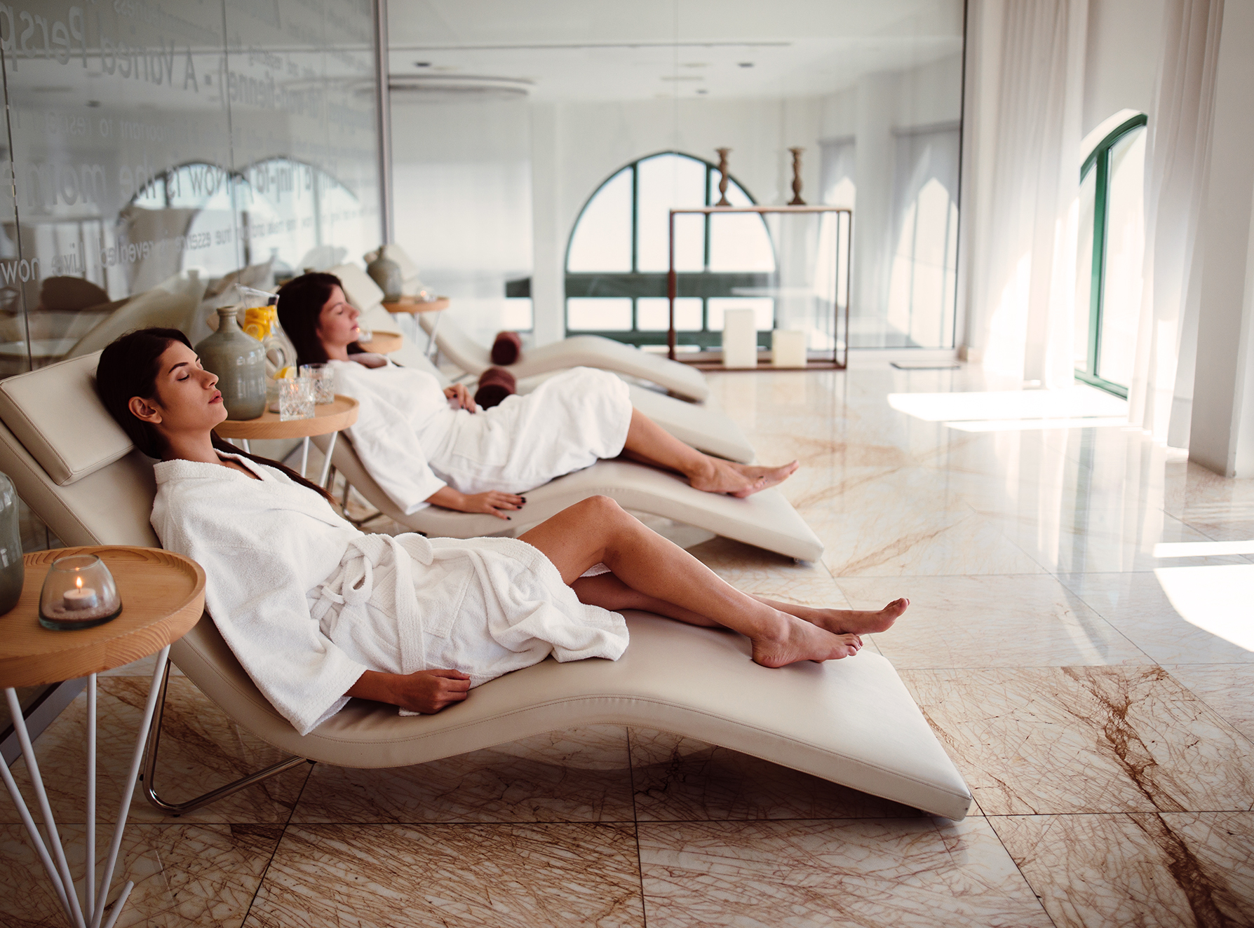 Two woman in white bath robes, relaxing in a high-end spa.